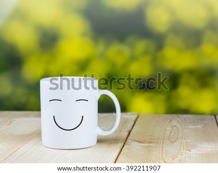 Smiley coffee cup on wood table with green bokeh background Royalty-Free Stock Photo #392211907