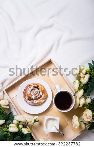 good morning - breakfast with sweet bun and tea on wooden tray and flowers in bed