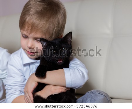 two happy young children: white-skinned boy blond girl sitting with a black cat and noutbukomego (brother and sister) on a white sofa watching cartoons with your computer