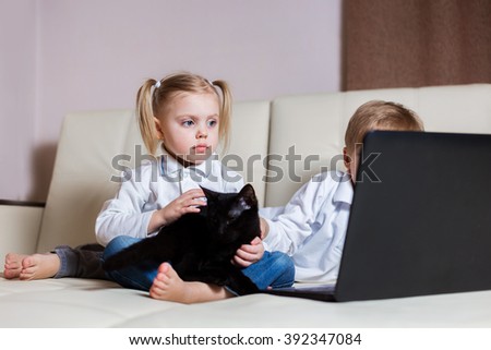 two happy little baby boy and a fair-skinned blonde girl (brother and sister) sitting on the floor with a laptop, looking at the picture and smile
