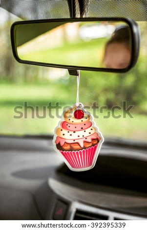 Cupcake shaped car freshener hanging on back view mirror inside car Royalty-Free Stock Photo #392395339