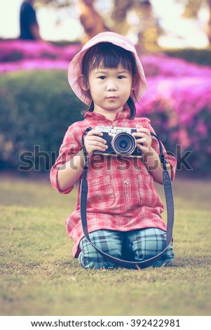 Cute little asian girl holding vintage film camera in the park on blurred background, summer in the day time. Adorable child in nature, outdoors. Vintage style.
