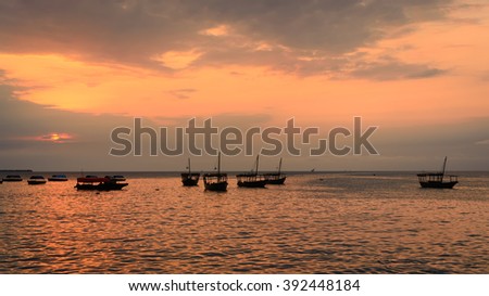 Colorful horizontal photo of traditional dhow boats on open sea on Indian Ocean close to Stone Town on Zanzibar, Tanzania in East Africa, at orange sunset.