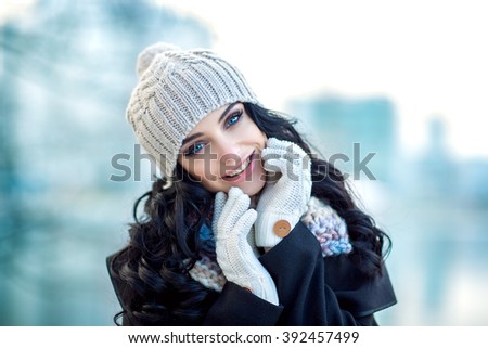 Beautiful woman portrait. Nice smile. Outside photo shoot. Winter. A girl is in warm clothes and with hat on head. Nice make up and curly hairs.