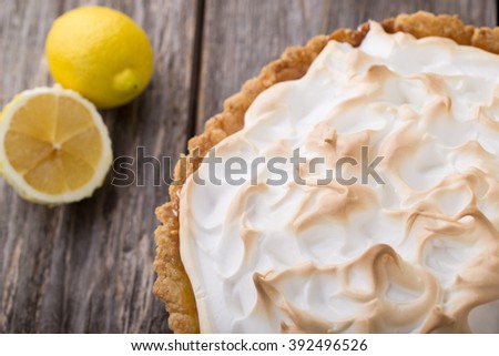 Lemon meringue pie on wooden table with lemons on background close up. Top view.