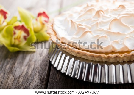 Whole lemon meringue pie on wooden desktop with orchids on background