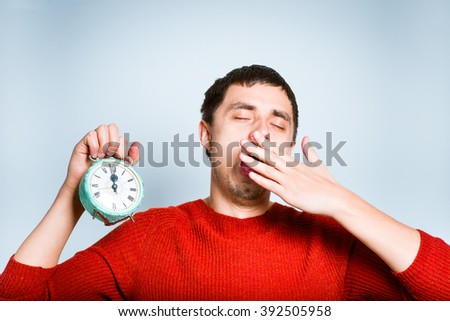 businessman yawning with a retro alarm clock isolated on a gray background