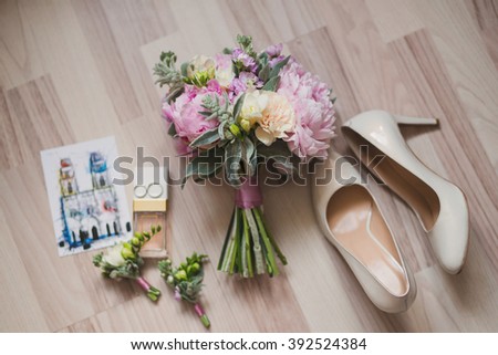 bouquet with peonies, boutonnieres, perfume, female leather shoes, paper card and wedding rings on light wooden background