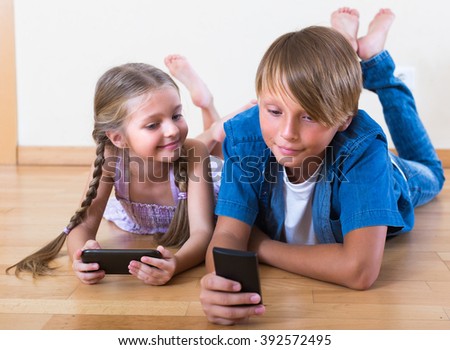 Smiling little girl and teenage boy burying in mobile phones laying on the floor
 Royalty-Free Stock Photo #392572495