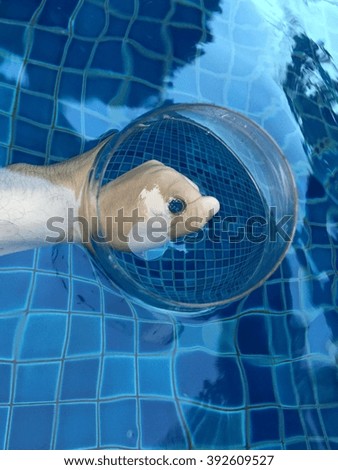 Hand of a man holding empty wine glass partly submerge in a pool, causing an illusion effect.