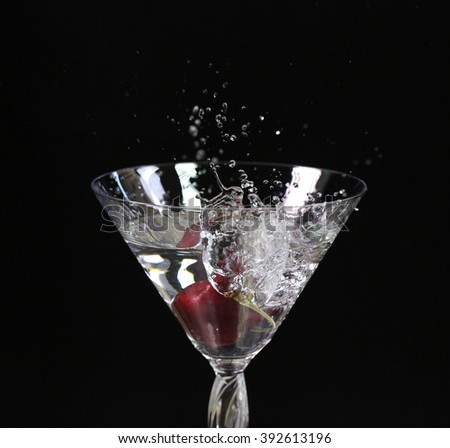 Red cherry fall into the water glass on black background
