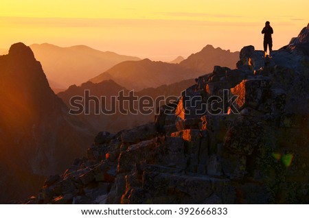 Silhouette of alone man on the top of rocky mountains in warm sunset light
