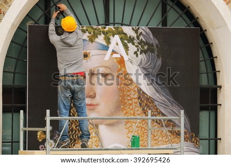 A worker hangs a large advertising poster on the facade of the house.