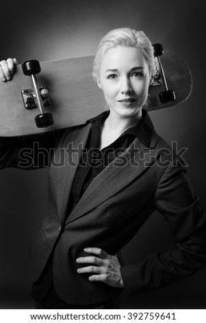 CLose up studio shot of a business woman holding a wooden skateboard.  Shot on a grey background.