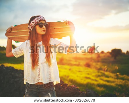 Beautiful young woman with skateboard on country road at sunset