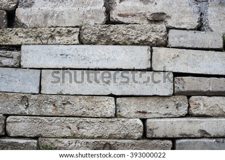 Old masonry made of artificial curb stone with patches of dry grass.