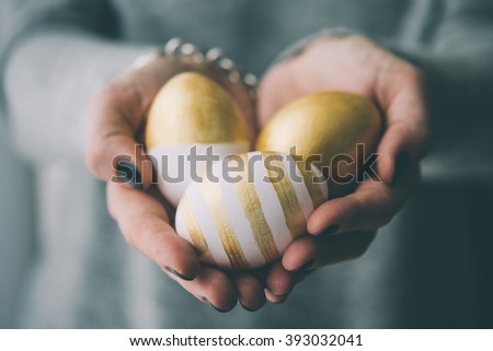 Hands holding modern  easter eggs painted in gold. Toned picture