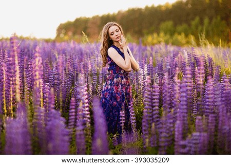 beautiful girl with flowers lupines in a field at sunset