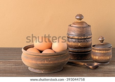  Chicken eggs in a wooden bowl and wooden utensils on a brown background.