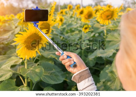 woman holding selfie stick taking photo at sunflower field