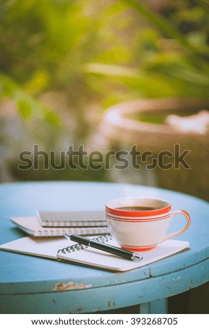Coffee cup with notebooks and pen on blue round wood table in morning time with vintage filter effect