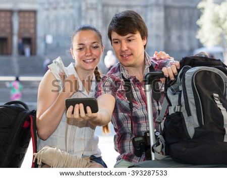 american couple with luggage doing selfie at travel destination background