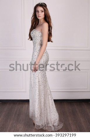 fashion photo of beautiful young woman with dark hair wears elegant dress and precious crown,posing in studio 
