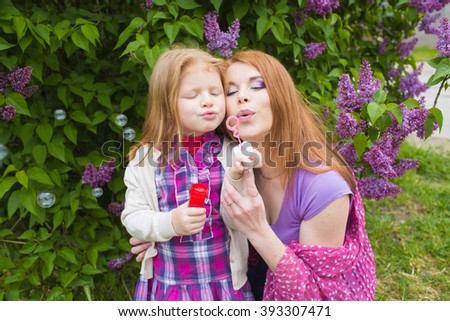 happy mother and daughter in the garden of blooming lilacs