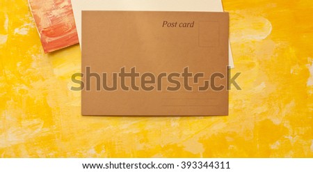 A brown paper blank postcard with a place for text, shot from above on painterly textures; the golden yellow page has additional copyspace