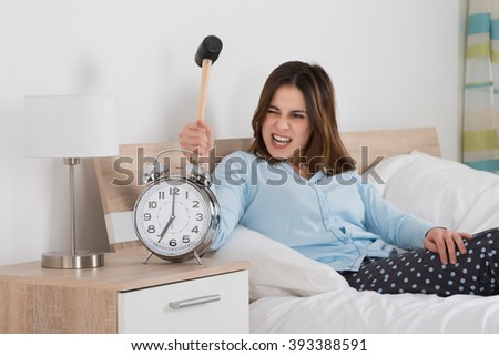Young Woman Smashing Alarm Clock With Hammer On Bed