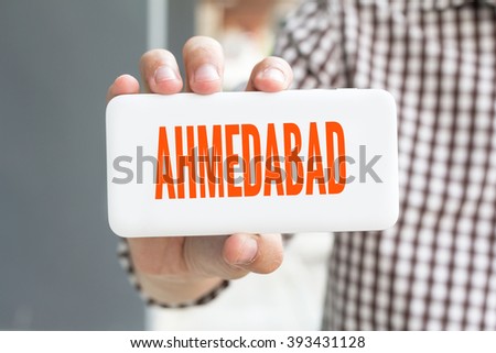 Man hand showing AHMEDABAD word phone with  blur business man wearing plaid shirt.