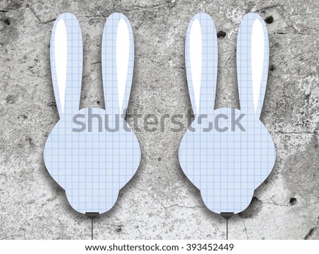 Close-up of two hanged blank rabbit silhouettes frames with small squares against grey weathered concrete wall background