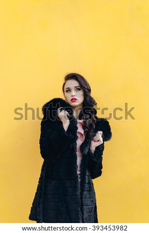 Beautiful girl in a black fur coat. Yellow background