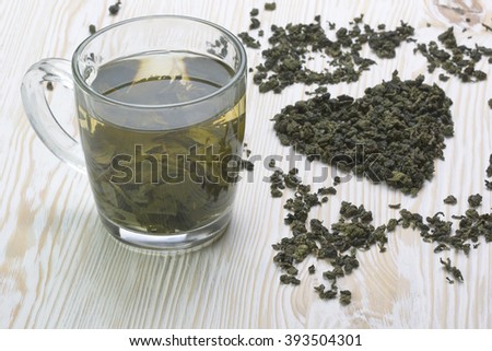 Green tea leaf in shape heart, mug on  wooden  background
