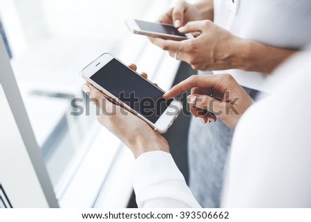 Closeup image of a woman`s hand is holding mobile phone with copy space screen for your advertising text message or promotional content, while her colleague is chatting in network on cell telephone