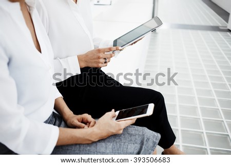 Closely of woman is dialing the number on mobile phone, while her partner near is reading electronic book on touch pad. Female is chatting on cellphone,while colleague next to her using digital tablet
