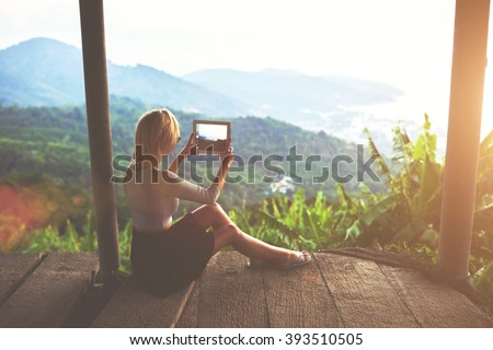 Female traveler is shooting video on portable touch of a wonderful Amazon view during her unforgettable summer weekend. Young woman tourist is taking photo with digital tablet camera of jungle view