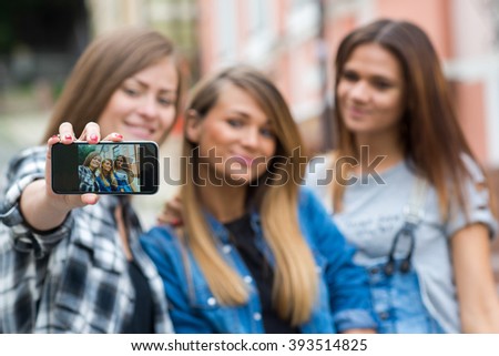 Best friends. Young friends girls are having fun together on the street and smile at each other. Beautiful girls friends are doing photo selfie on mobile cell phone