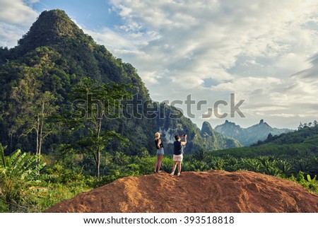 Back view of a woman is taking photo with cell telephone camera of an amazing jungle landscape. Female is shooting video on mobile phone during summer weekend with her daughter in Thailand