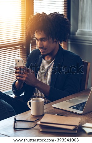 Important message. Young handsome African man using his smartphone while sitting at his working place