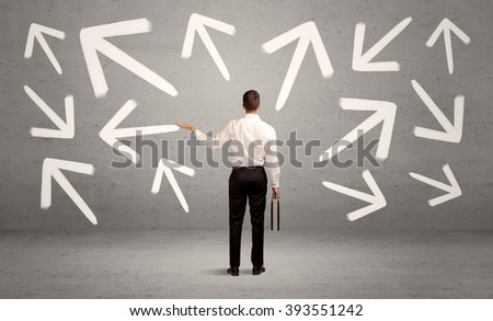 An elegant businessman standing with his back in front of urban wall full of arrows pointing in different directions concept