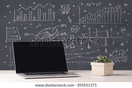 An elegant office desktop with portable laptop and drawn pie charts, graphs, numbers in the background concept