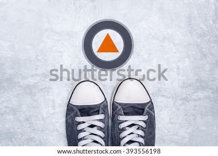 Young man in casual canvas shoes standing on concrete road, modern direction arrow sign, top view.