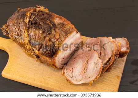 Roasted rolled pork meat on a cutting board on a black table