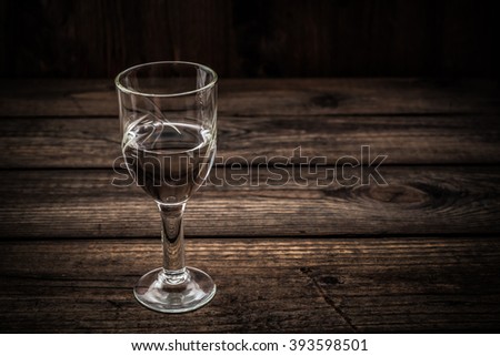 Glass of vodka on an old wooden table. Angle view, image vignetting and hard tones