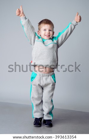 Happy boy showing sign okay with fingers. He with blond hair and dressed in a grey sports suit. Sporting style. Studio shot