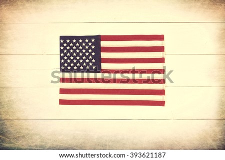 Red, White and Blue American Flag in Center on Rustic Wood Boards Background.  Horizontal rectangle is cross processed with warm sepia toned vintage treatment for retro look and with dark vignette.