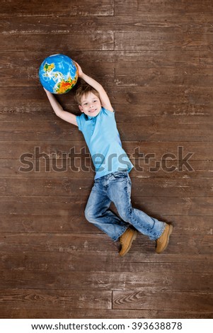 Happy child. Top view creative photo of little boy on vintage brown wooden floor. Boy holding globe, looking at camera and smiling