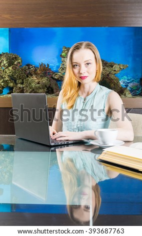 Beautiful woman with laptop and book in front of aquarium