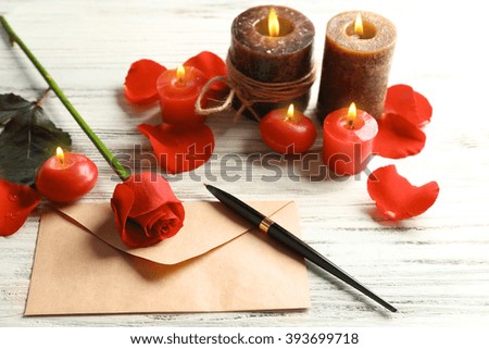 Gift card for Valentine's Day with pen, red rose and candles on white wooden background